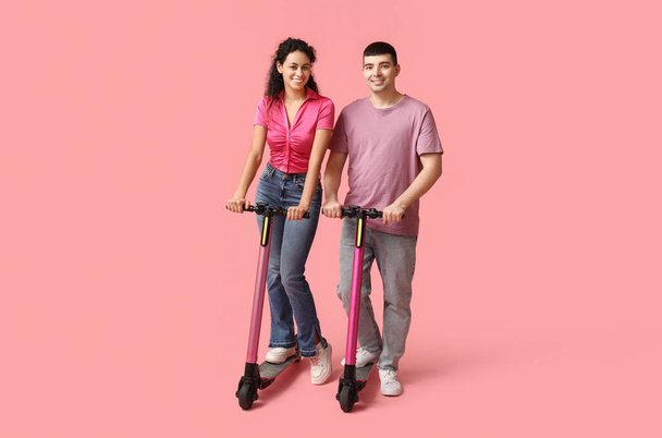 Beau jeune couple avec des scooters électriques modernes coup de pied sur fond rose - Photo, image