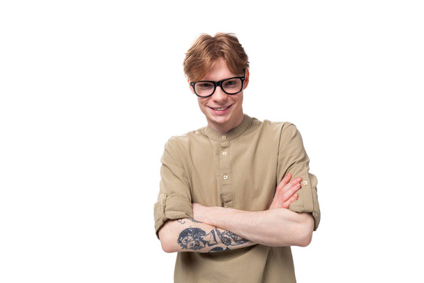 joven hombre guapo con pelo de cobre con un tatuaje en el brazo lleva una camisa marrón. - Foto, imagen