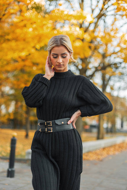 Krásná elegantní mladá blondýnka v módní černé pletené šaty procházky v podzimním městském parku se zlatým listím - Fotografie, Obrázek