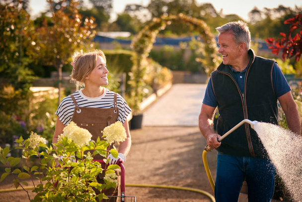 Mature Man And Woman Working Outdoors In Garden Centre Watering Plants - Foto, Imagem
