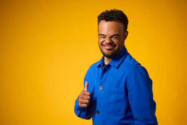 Studio Portrait Of Man With Down Syndrome Standing Against Yellow Background Giving Thumbs Up - Фото, изображение