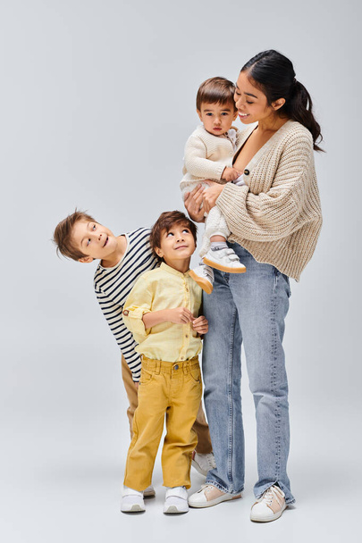 A young Asian mother stands next to her children, in a studio setting with a grey background. - Photo, Image