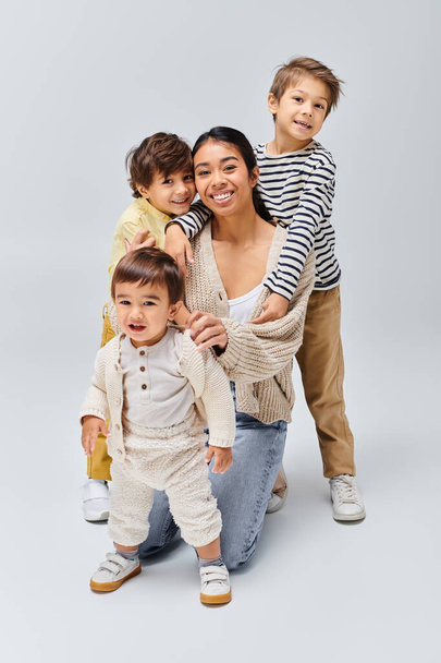 Una joven madre asiática y sus hijos adoptan una pose encantadora en un estudio sobre un fondo gris. - Foto, imagen