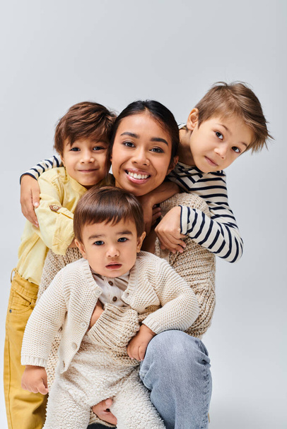 Um grupo de crianças felizes posando juntas em um estúdio para sua jovem mãe asiática em um fundo cinza. - Foto, Imagem