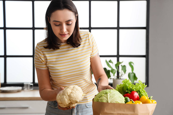Молода жінка з паперовим мішком зі свіжих овочів на кухні - Фото, зображення