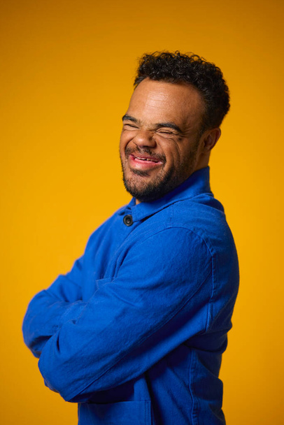 Studio Portrait Of Smiling Man With Down Syndrome Standing Against Yellow Background - Foto, Imagem