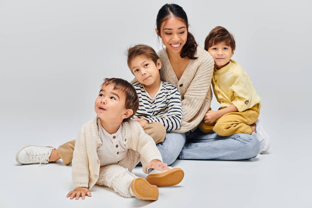 Una giovane madre asiatica siede a terra con i bambini, creando un momento sereno di unità e connessione.. - Foto, immagini