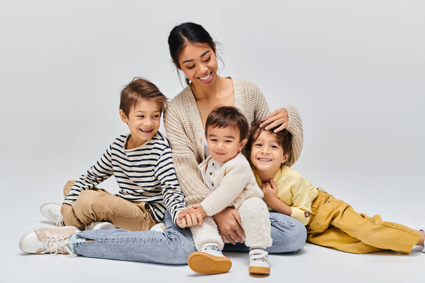 Uma jovem mãe asiática sentada no chão com seus filhos, interagindo e criando um vínculo especial em um estúdio. - Foto, Imagem
