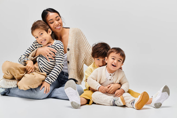 Uma jovem mãe asiática se senta no chão com seus filhos, compartilhando um momento de conexão e amor em um estúdio. - Foto, Imagem