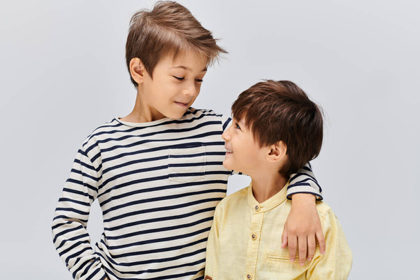 Двоє молодих азіатських хлопчиків стоять пліч-о-пліч у студії на сірому фоні. - Фото, зображення