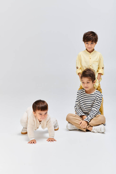 Trois jeunes garçons sont assis paisiblement sur le sol devant un fond blanc, respirant un sentiment de calme. - Photo, image