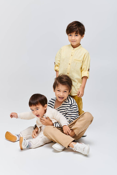 Trójka dzieci, siedząca na podłodze, angażuje się w zabawną interakcję ze sobą w przytulnym studio. - Zdjęcie, obraz
