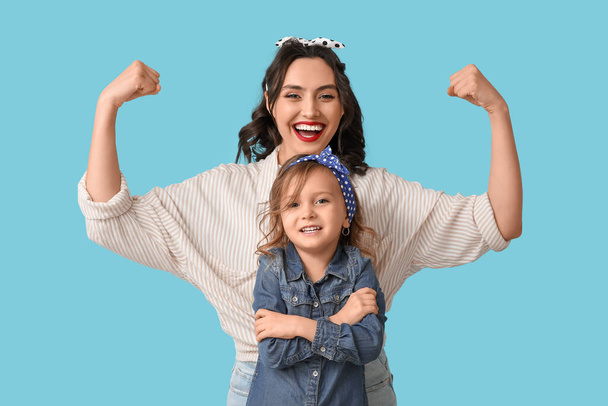 Beautiful pin-up woman showing muscles and her daughter on blue background - Photo, Image
