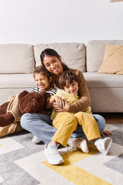 Eine junge asiatische Mutter sitzt mit ihren beiden kleinen Söhnen im gemütlichen Wohnzimmer zu Hause auf dem Boden. - Foto, Bild
