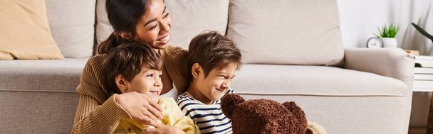 Mladá asijská matka sedí na gauči se svými dvěma malými syny v útulném obývacím pokoji. - Fotografie, Obrázek