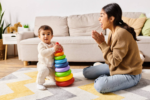 Młoda azjatycka matka z radością angażuje się ze swoim synkiem na podłodze ich przytulnego salonu. - Zdjęcie, obraz