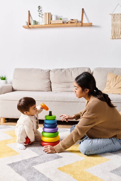 Egy fiatal ázsiai anya boldogan játszik a kisfiával a padlón a kényelmes nappalijában.. - Fotó, kép