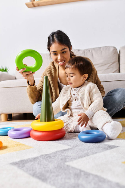 Una joven madre asiática interactúa alegremente con su pequeño hijo en el suelo de su sala de estar en casa. - Foto, Imagen