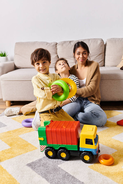 Молодая азиатская мать и два ее сына счастливо играют с игрушечным грузовиком в своей гостиной. - Фото, изображение