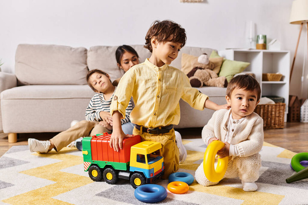 Eine Gruppe von Kindern, darunter die kleinen Söhne einer jungen asiatischen Mutter, spielen fröhlich mit Spielzeug in einem warmen und einladenden Wohnzimmer. - Foto, Bild
