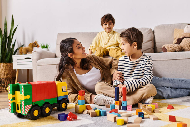 Una joven madre asiática sentada en el suelo, jugando alegremente con sus pequeños hijos en la acogedora sala de estar de su casa. - Foto, Imagen