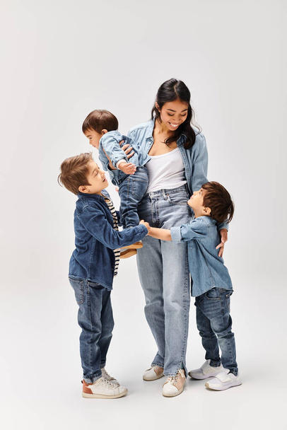 Junge asiatische Mutter und ihre drei Söhne, alle in Jeans gekleidet, stehen vereint vor einem schlichten weißen Hintergrund. - Foto, Bild