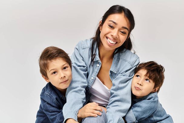 A young Asian mother sits on top of her two little sons, all wearing denim clothes in a grey studio setting. - Photo, Image