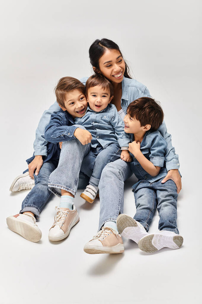 A young Asian mother sits majestically on a group of children, all wearing denim clothes, in a grey studio setting. - Photo, Image