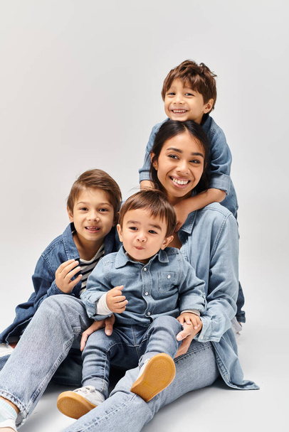 Uma jovem mãe asiática e seus filhinhos brincam em cima uns dos outros, todos vestindo roupas de ganga em um estúdio cinza. - Foto, Imagem