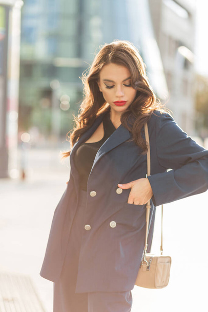 Bela moda urbana retrato feminino de uma menina de negócios elegante bastante elegante em um terno azul elegante com um saco caminha na cidade em um dia ensolarado. Senhora da moda - Foto, Imagem