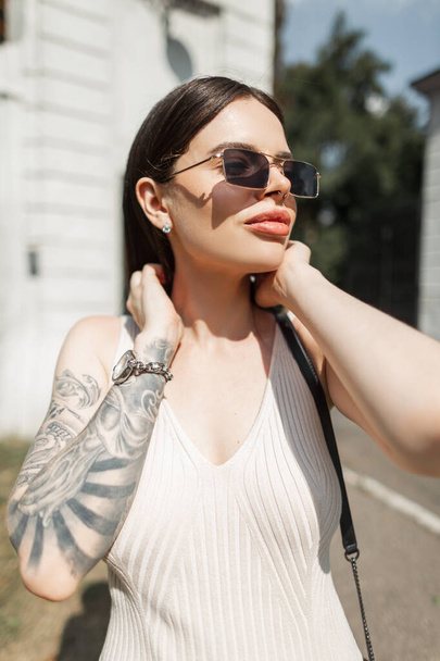 Mode urbaine été beau modèle de femme avec des lunettes de soleil avec tatouage sur le bras dans des promenades élégantes robe beige dans la journée ensoleillée d'été. Jolie fille - Photo, image