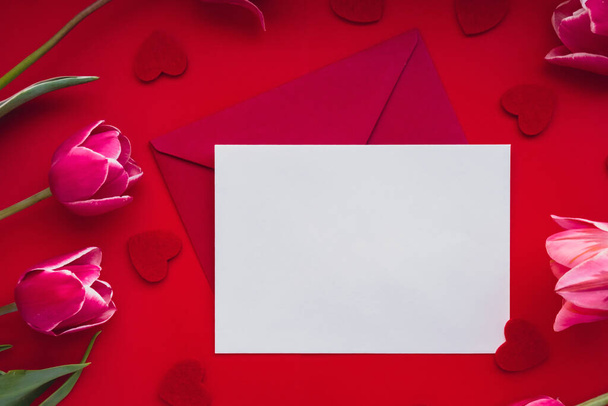 Pusta biała koperta kopiuj miejsce na tekst lub projekt z pięknym różowym bukietem tulipanowym na czerwonym tle. Czerwone serduszko. Miłość romantyczna Walentynki. makieta szablonu świątecznego wiosennego powitania - Zdjęcie, obraz
