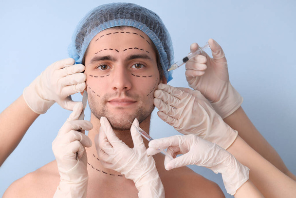Cirujanos plásticos con herramientas y hombre joven con la cara marcada sobre fondo azul, primer plano - Foto, imagen