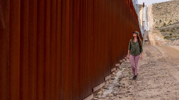 Απελπισμένος μετανάστης πλοηγείται στο συνοριακό τείχος της Γιακούμπα, επιδιώκοντας παράνομη είσοδο στις Ηνωμένες Πολιτείες, τονίζοντας τις συνεχιζόμενες μεταναστευτικές προκλήσεις - Φωτογραφία, εικόνα