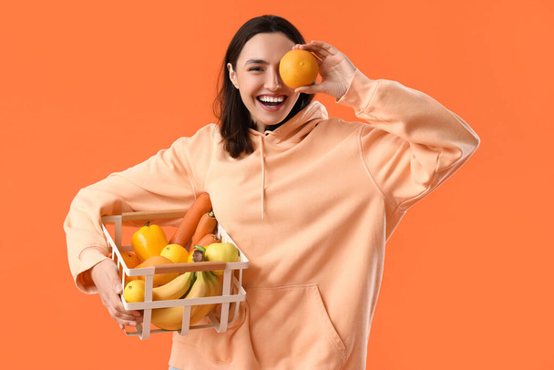 Mujer joven con cesta de comida saludable sobre fondo naranja - Foto, Imagen