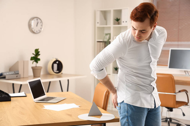 Young businessman and thumbtack on table in office. Hemorrhoids concept - Photo, Image