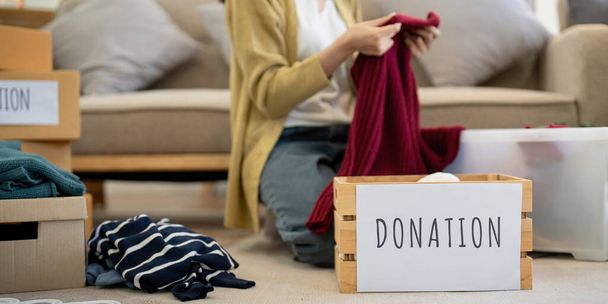 Darování, asijská mladá žena sedící doma, oblékání věcí do dárcovské krabice s použitým oblečením, charitativní pomoc a potřební lidé. Opětovné použití. - Fotografie, Obrázek