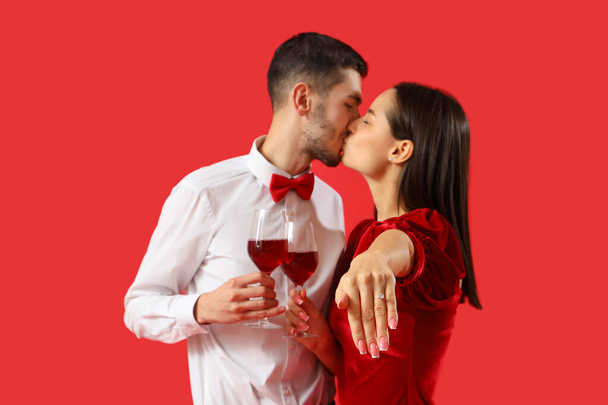 Szczęśliwa młoda para z kieliszkami wina całuje się na czerwonym tle. Święto Walentynek - Zdjęcie, obraz