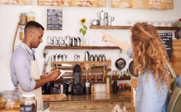 Barista, cafe and customer service with drink, order and menu for choice, writing and helping. Small business owner, cashier or waiter listening to person for decision on sale and coffee shop startup. - Photo, Image