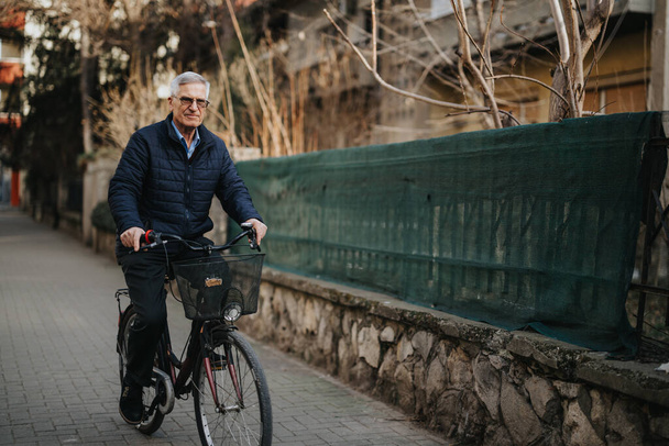 Um adulto idoso ativo está pedalando em uma estrada urbana, retratando estilo de vida saudável e lazer na aposentadoria. A imagem evoca um sentimento de contentamento e bem-estar. - Foto, Imagem