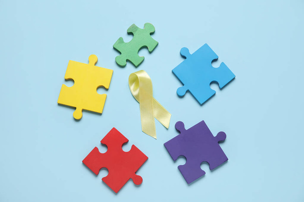 Zlatá stuha s kousky puzzle na modrém pozadí. Koncept povědomí o rakovině v dětství - Fotografie, Obrázek