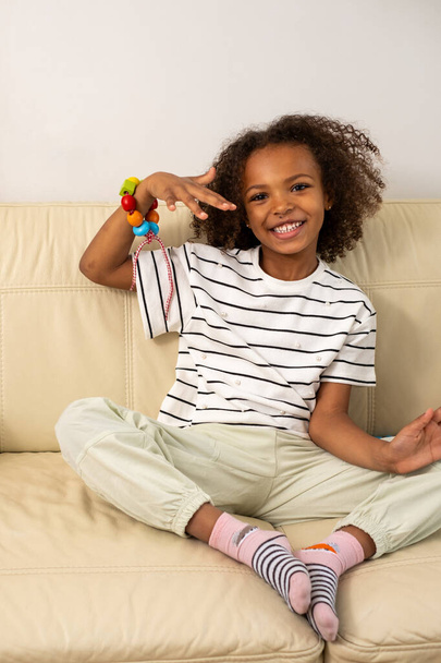 Een mooi, gelukkig en lachend gemengd ras meisje speelt met houten speelgoed op een beige bank symboliseert kleuteronderwijs en creatieve activiteiten. Hoge kwaliteit foto - Foto, afbeelding
