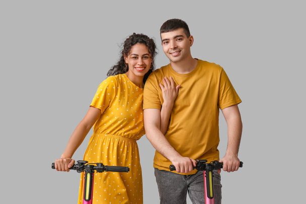 Jovem casal feliz com scooters modernos pontapé elétrico no fundo cinza - Foto, Imagem