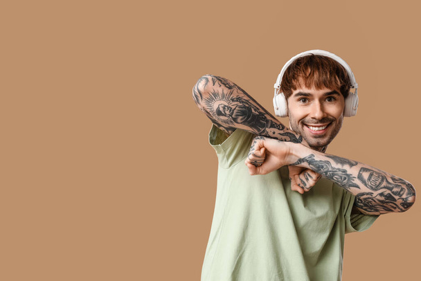 Nuori tatuoitu mies kuulokkeet tanssia vastaan beige tausta - Valokuva, kuva
