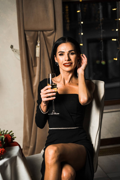 Розкішна жінка в чорній сукні обідає в ресторані з квітами та келихом шампанського. Романтична вечеря. Міжнародна концепція жіночого дня - Фото, зображення