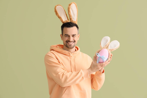 Jeune homme aux oreilles de lapin et oeuf de Pâques sur fond vert - Photo, image