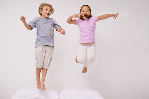 Springen, bed en kinderen met plezier, energie en ochtend in een slaapkamer met spel en broer / zus. Jeugd, hop en thuis met een opgewonden kinderen op een dekbed in de lucht met gek spel en spring in huis met vrienden. - Foto, afbeelding
