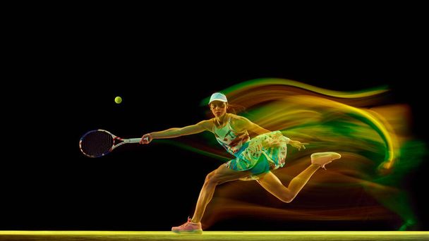 Dynamic action photo of young woman, tennis αθλητής με πολύχρωμη, ζωηρή κίνηση θολούρα σε μαύρο φόντο στούντιο. Έννοια των γυναικών στον αθλητισμό, ενεργό τρόπο ζωής, τουρνουά, ενέργεια, κίνηση. - Φωτογραφία, εικόνα