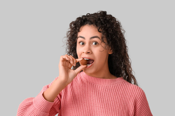 Όμορφη νεαρή Αφρο-Αμερικανίδα γυναίκα τρώει γλυκά σοκολατένια γλυκά σε γκρι φόντο - Φωτογραφία, εικόνα