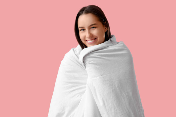 Красивая молодая женщина завернутая в одеяло на розовом фоне - Фото, изображение